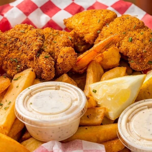 Crispy fried shrimp and french fries in a take-out container with lemon wedges and dipping sauces.