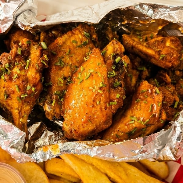 Crispy chicken wings with herbs in a foil-lined container, alongside golden french fries.